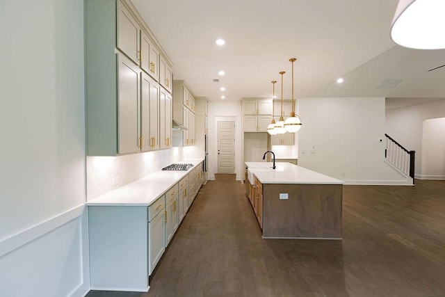 kitchen featuring decorative light fixtures, stainless steel gas cooktop, a center island with sink, light countertops, and a sink