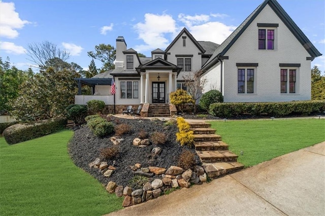 view of front facade with a front yard, a chimney, french doors, and brick siding