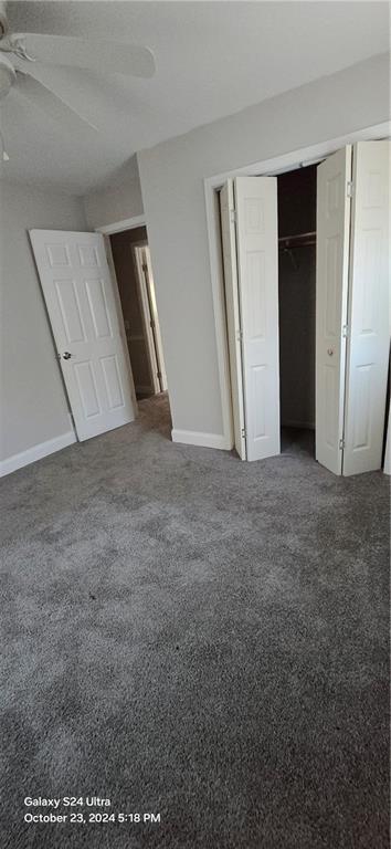 unfurnished bedroom featuring ceiling fan, dark carpet, and a closet