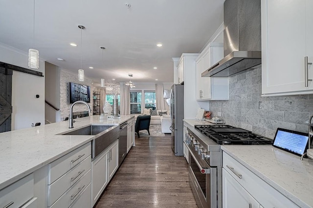 kitchen with ornamental molding, a sink, white cabinetry, appliances with stainless steel finishes, and wall chimney range hood