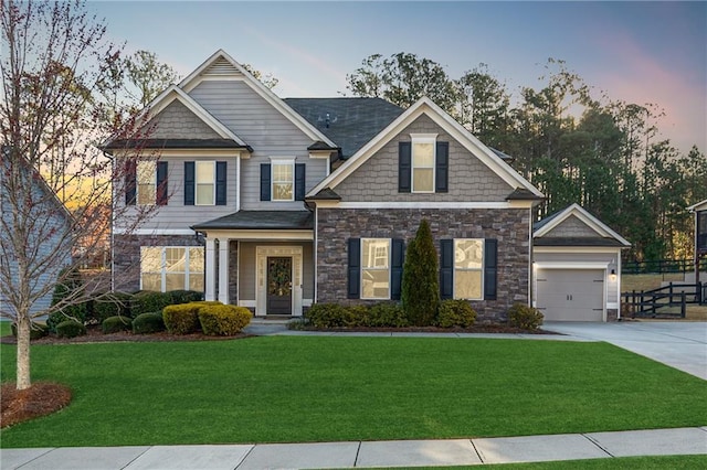 craftsman-style home featuring concrete driveway, a garage, a front yard, and stone siding