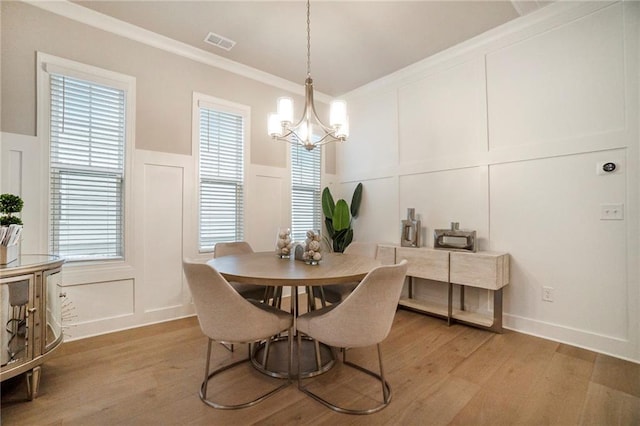 dining room with a chandelier, visible vents, light wood finished floors, and a decorative wall
