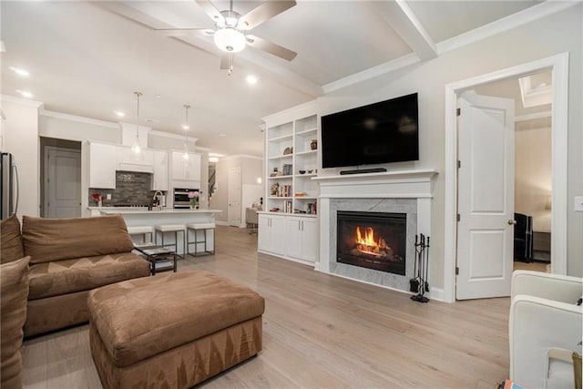 living area with crown molding, ceiling fan, light wood-type flooring, recessed lighting, and a premium fireplace