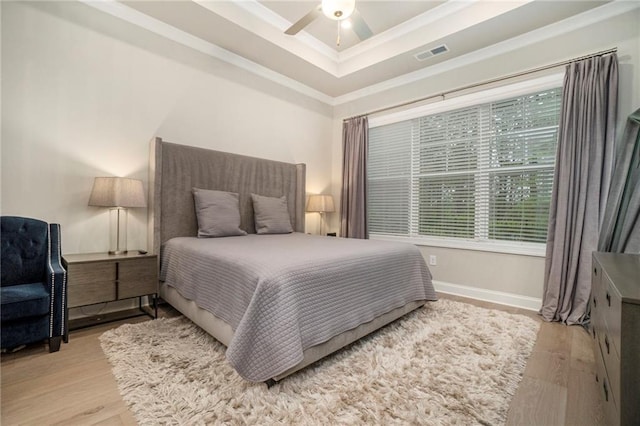 bedroom with a raised ceiling, ornamental molding, light wood-style flooring, and visible vents