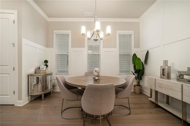 dining room featuring an inviting chandelier, ornamental molding, wainscoting, visible vents, and a decorative wall