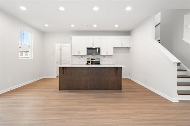 kitchen featuring white cabinetry, an island with sink, light hardwood / wood-style floors, and appliances with stainless steel finishes