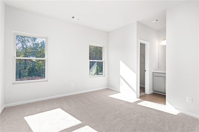 unfurnished bedroom featuring ensuite bathroom, light carpet, and a spacious closet