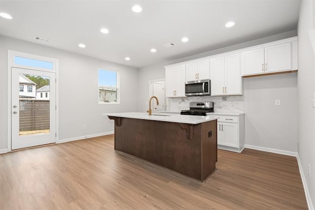 kitchen with white cabinets, light hardwood / wood-style flooring, stainless steel appliances, and an island with sink