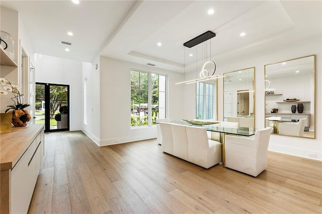 dining area featuring light wood-type flooring and a raised ceiling