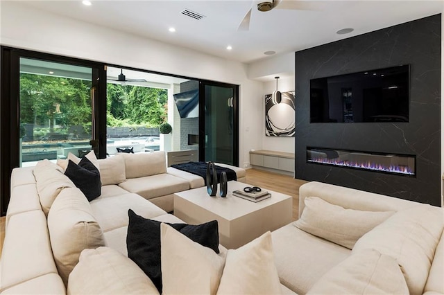 living room with wood-type flooring, ceiling fan, and a high end fireplace