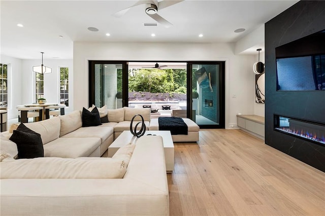 living room with ceiling fan, a tile fireplace, and light hardwood / wood-style flooring