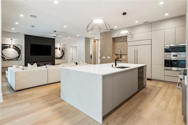 kitchen featuring light hardwood / wood-style flooring, hanging light fixtures, sink, a center island with sink, and stainless steel appliances