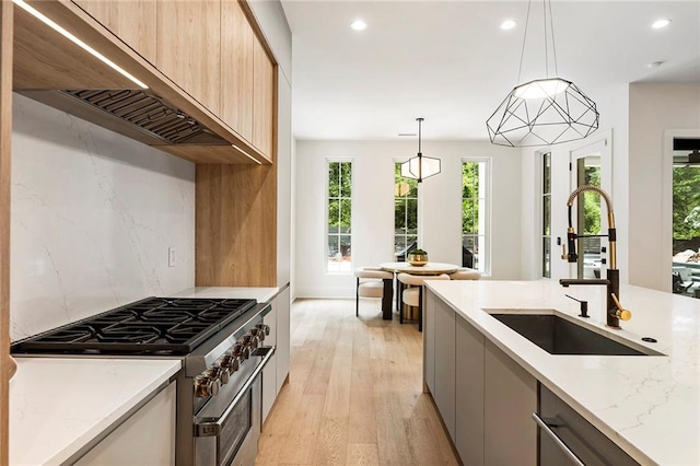 kitchen featuring decorative light fixtures, custom exhaust hood, sink, light stone counters, and stainless steel appliances