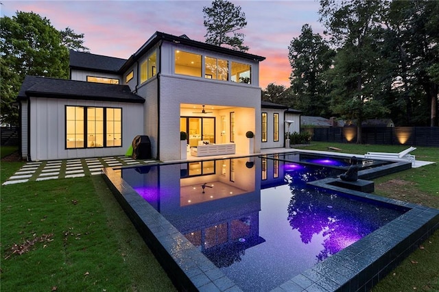 back house at dusk with a pool with hot tub, a patio area, and a lawn