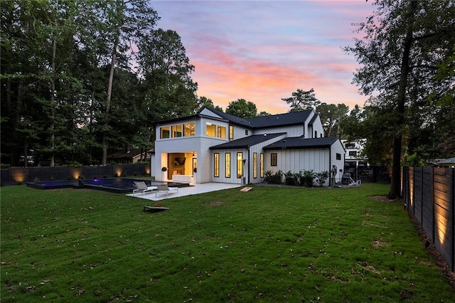 back house at dusk featuring a yard and a patio