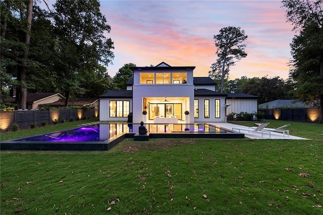 back house at dusk with a fenced in pool and a yard