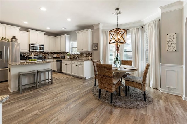 dining space featuring sink, ornamental molding, light hardwood / wood-style floors, and a chandelier