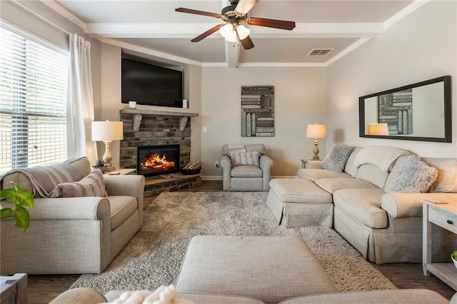 living room featuring a stone fireplace, beamed ceiling, hardwood / wood-style flooring, ornamental molding, and ceiling fan