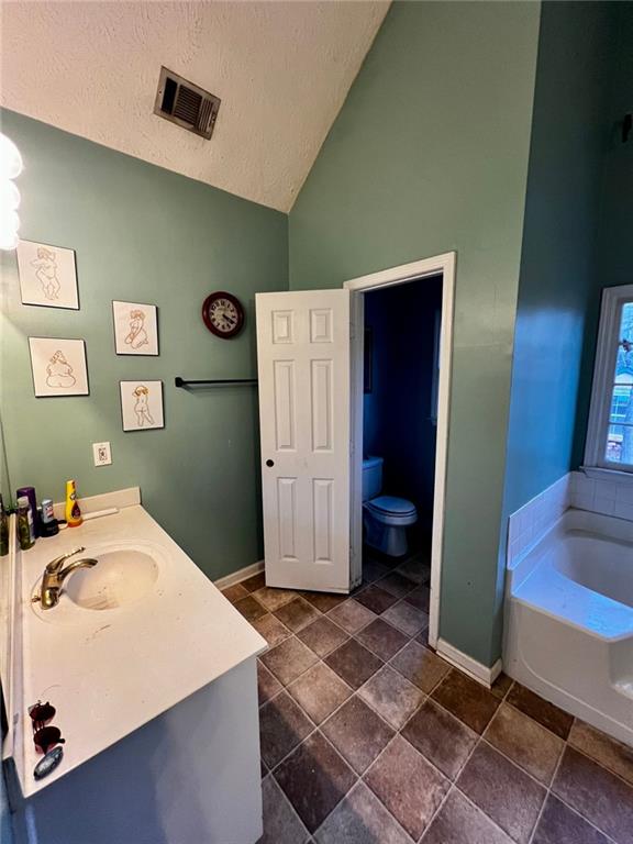 bathroom featuring a washtub, vanity, a textured ceiling, vaulted ceiling, and toilet