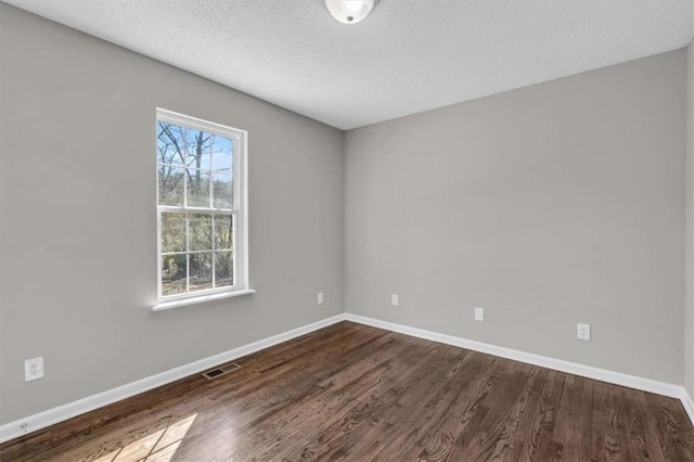 unfurnished room with a textured ceiling, dark wood finished floors, visible vents, and baseboards