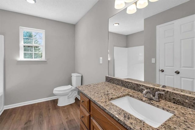 bathroom featuring toilet, wood finished floors, vanity, baseboards, and a shower