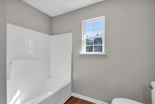 bathroom featuring washtub / shower combination, baseboards, toilet, and wood finished floors