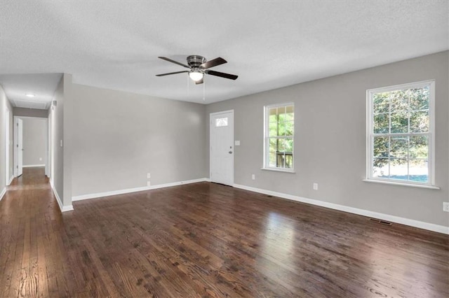 unfurnished living room with ceiling fan, a textured ceiling, visible vents, baseboards, and dark wood-style floors