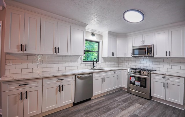 kitchen with light stone counters, white cabinets, sink, appliances with stainless steel finishes, and dark hardwood / wood-style flooring