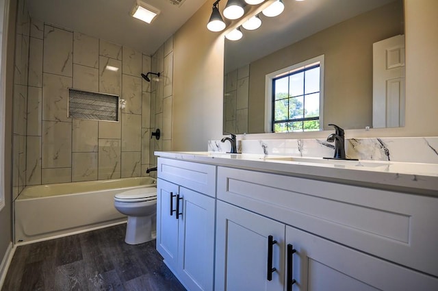 full bathroom with wood-type flooring, tiled shower / bath, vanity, and toilet