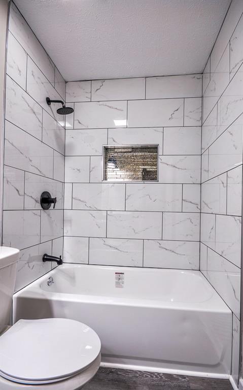 bathroom featuring a textured ceiling, toilet, and tiled shower / bath