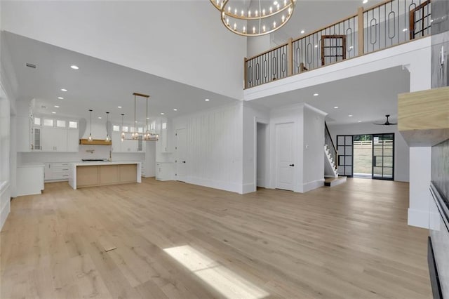 3893 Indian Shoals Rd, Dacula, GA 30019 - unfurnished living room featuring a chandelier, a towering ceiling, stairway, light wood-style floors, and a ceiling fan
