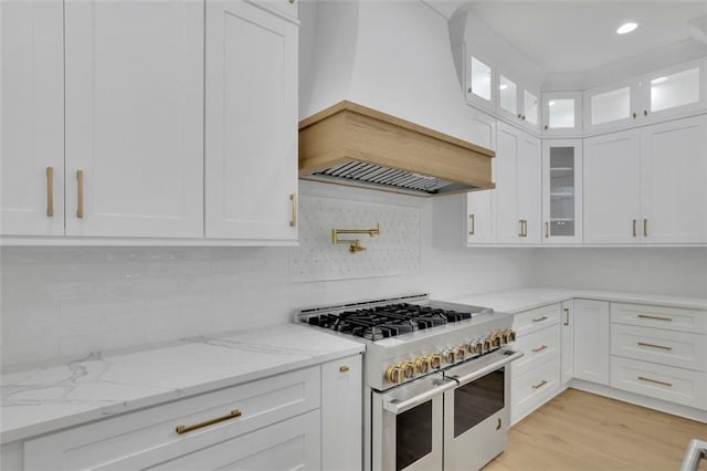 3893 Indian Shoals Rd, Dacula, GA 30019 - kitchen with range with two ovens, premium range hood, white cabinetry, light stone counters, and glass insert cabinets