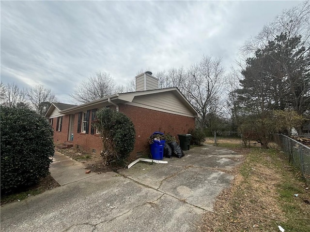 view of home's exterior featuring driveway, a chimney, crawl space, fence, and brick siding