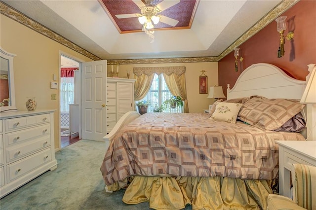 carpeted bedroom with a tray ceiling, ceiling fan, and ornamental molding