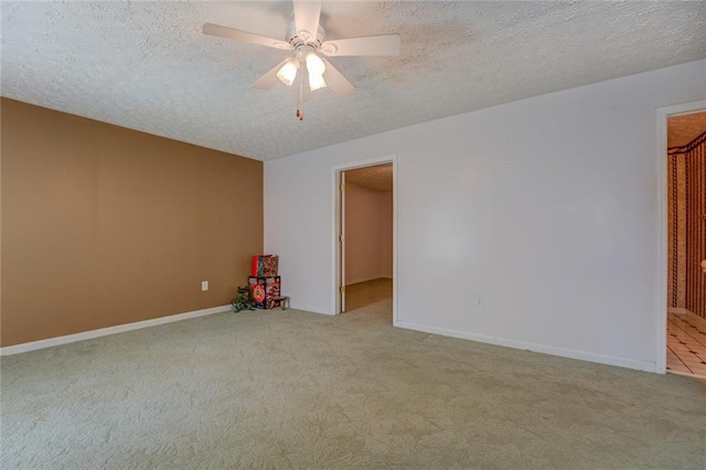 carpeted spare room with a textured ceiling, a ceiling fan, and baseboards