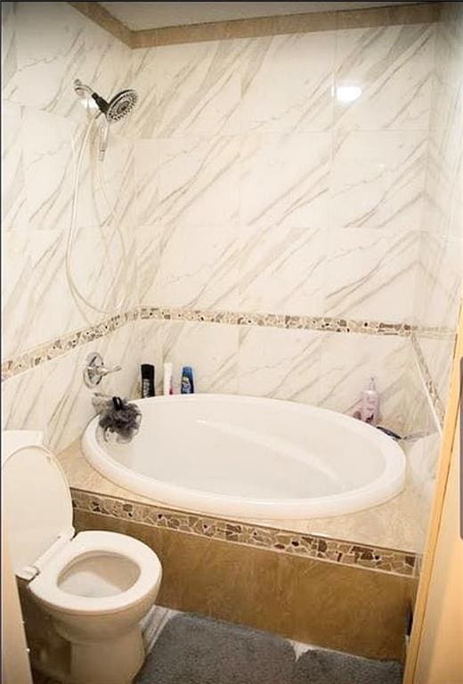 bathroom with tile walls, toilet, and tiled shower / bath