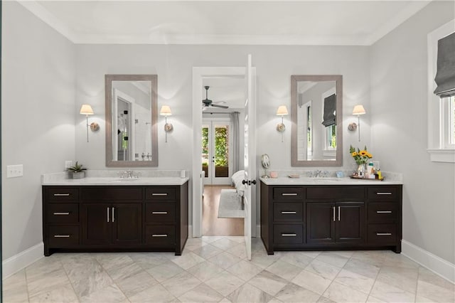 bathroom featuring a ceiling fan, baseboards, two vanities, marble finish flooring, and crown molding