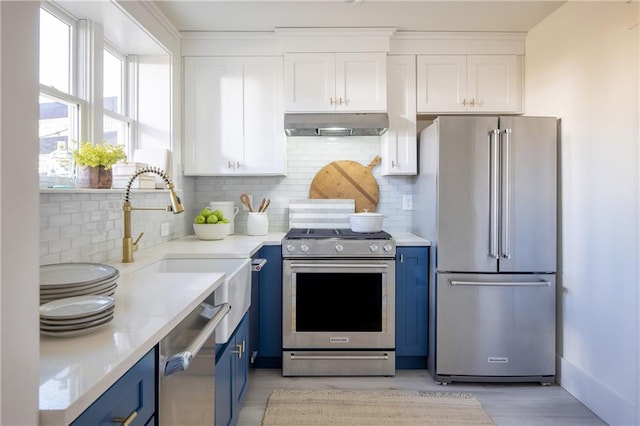 kitchen featuring stainless steel appliances, blue cabinetry, under cabinet range hood, white cabinetry, and decorative backsplash