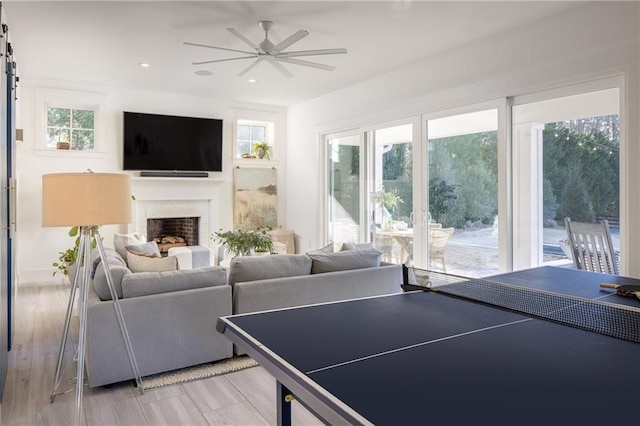 recreation room featuring a ceiling fan, a fireplace, and light wood-type flooring