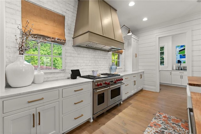 kitchen featuring double oven range, custom exhaust hood, light countertops, light wood finished floors, and recessed lighting