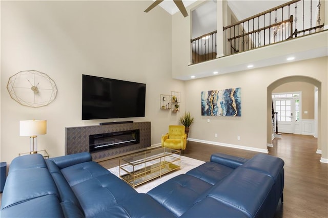 2055 Beacon Hill Way, Alpharetta, GA 30005 - living room with arched walkways, wood finished floors, ceiling fan, a glass covered fireplace, and a high ceiling