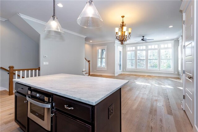 kitchen with ornamental molding, stainless steel oven, ceiling fan with notable chandelier, pendant lighting, and light hardwood / wood-style floors