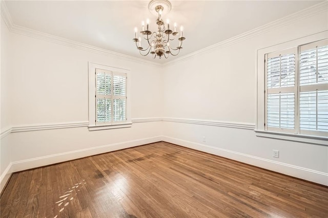 spare room with crown molding, a notable chandelier, wood finished floors, and baseboards