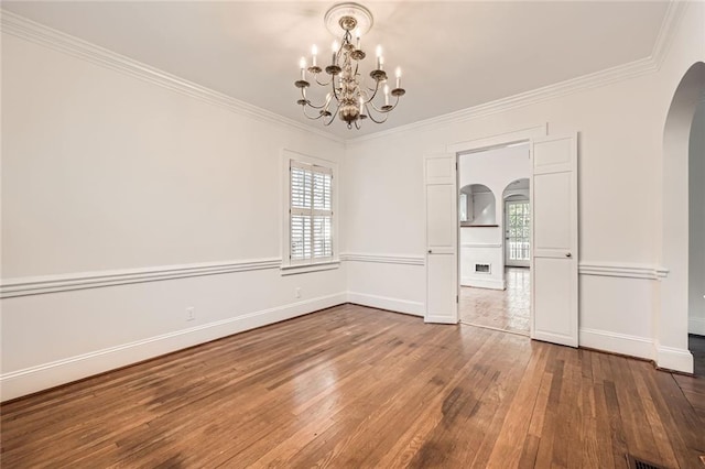 empty room with arched walkways, ornamental molding, baseboards, and hardwood / wood-style floors