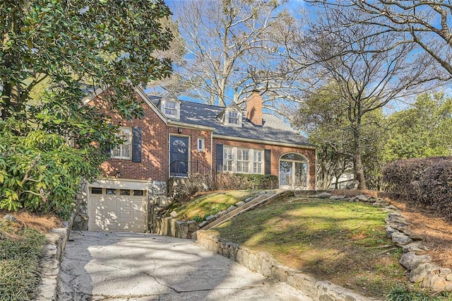 new england style home with brick siding, an attached garage, concrete driveway, and a chimney