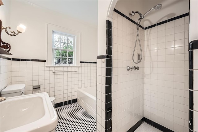 bathroom with tiled shower, toilet, tile walls, and a sink