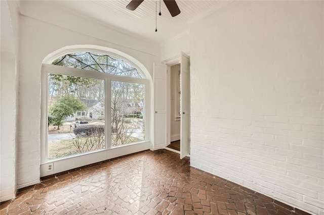 interior space with plenty of natural light, a ceiling fan, brick floor, and brick wall