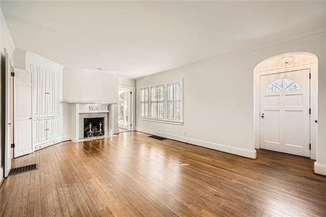 unfurnished living room featuring a high end fireplace, baseboards, wood-type flooring, and ornamental molding