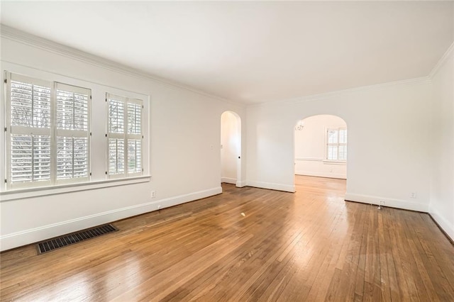 unfurnished room with visible vents, arched walkways, wood-type flooring, and crown molding