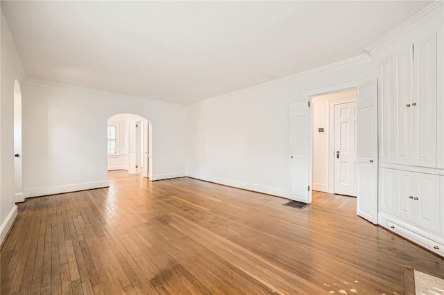 unfurnished room with arched walkways, light wood-type flooring, baseboards, and ornamental molding